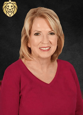 A smiling woman with blonde hair, wearing a red top, sits in front of a dark background featuring the Lyon Property Group’s gold lion logo, representing expert property management in Rhode Island and Eastern Connecticut.