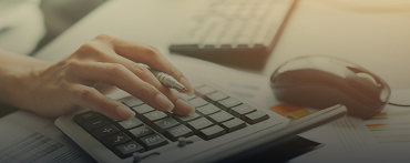 A person’s hand using a calculator on a desk, with a pen in hand, next to a computer mouse, keyboard, and documents at Lyon Property Group—your trusted choice for Property Management in Rhode Island and Eastern Connecticut.