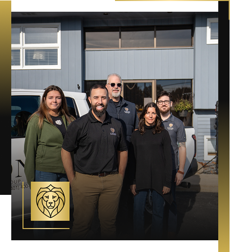 A group of five people, three men and two women, stand together outside a blue building next to a white vehicle. They are smiling in casual business attire. A gold lion logo for Lyon Property Group is at the bottom left corner.