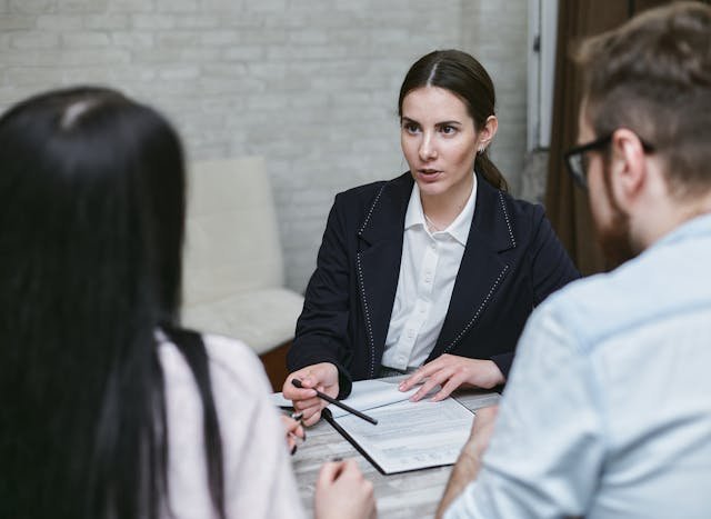 A woman in business attire sits at a table with two people, discussing documents and holding a pen, suggesting a formal meeting or consultation for Lyon Property Group’s property management services in Rhode Island and Eastern Connecticut.