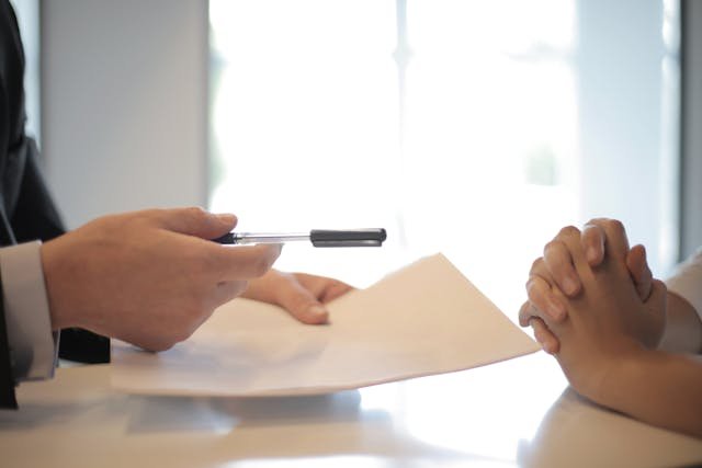 A person in a suit hands a pen and documents to another, suggesting a signing or agreement in a professional setting—reflecting Lyon Property Group’s commitment to property management in Rhode Island and Eastern Connecticut.